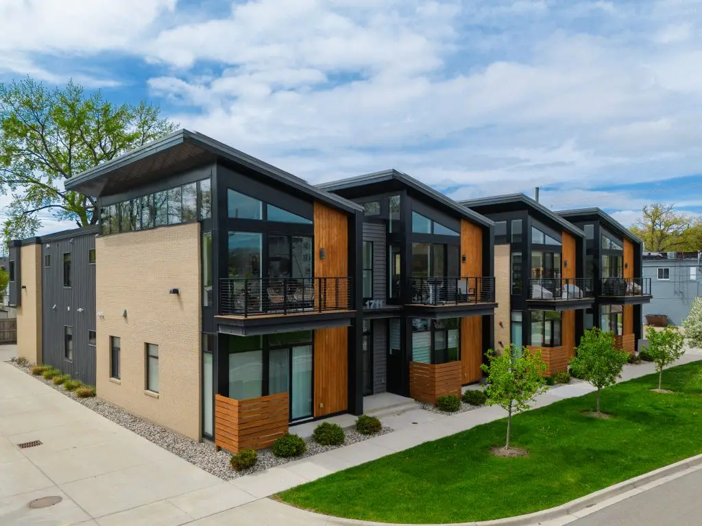 Angled view of modern two-story townhomes with a blend of brick, wood, and steel finishes, private balconies, and clean landscaping.