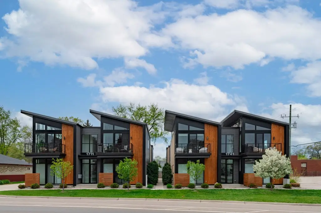 Contemporary townhome complex featuring sharp rooflines, wood panel accents, and floor-to-ceiling windows in a symmetrical four-unit layout.