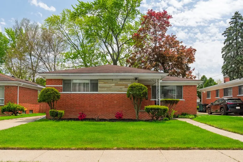 Brick ranch-style home with mid-century stone accents, manicured lawn, and mature trees in a quiet suburban Metro Detroit neighborhood.