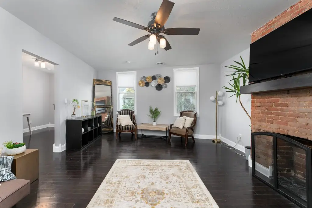 Bright and modern living room with dark hardwood floors, exposed brick fireplace, and mid-century furnishings in a Pittsburgh rowhome.
