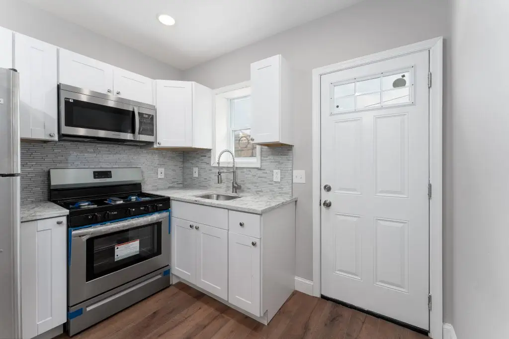 Contemporary kitchen with white shaker cabinets, stainless steel appliances, tile backsplash, and a rear entry door in a Philadelphia rowhome.