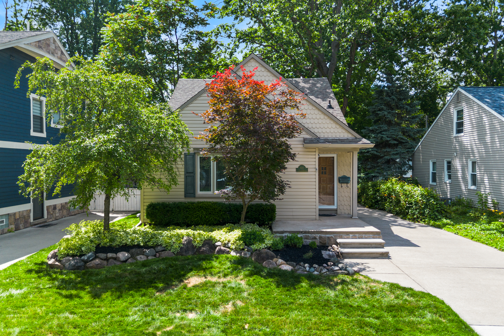 Front exterior of a Royal Oak character home with layered rooflines, mature trees, landscaped front yard, and driveway.