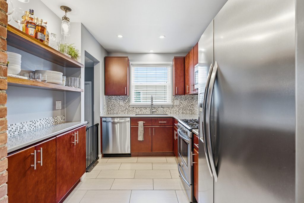 Long view through a Royal Oak galley kitchen with wood cabinetry, stainless appliances, open shelving, and window over the sink.