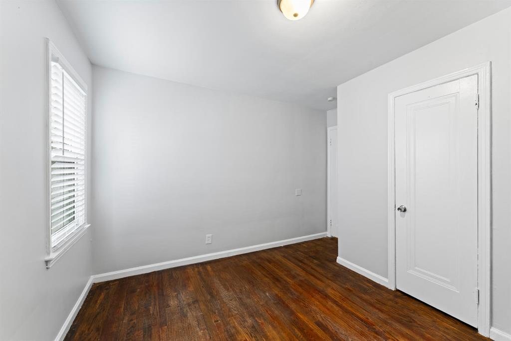 Vacant bedroom with side window, hardwood flooring, white closet door, gray walls, and an opening to the hall.