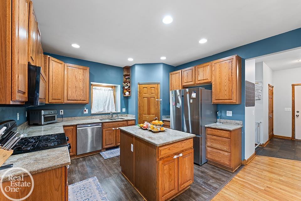 St. Clair Shores kitchen with wood cabinetry, stainless appliances, center island, blue walls, and open connection to entry area.