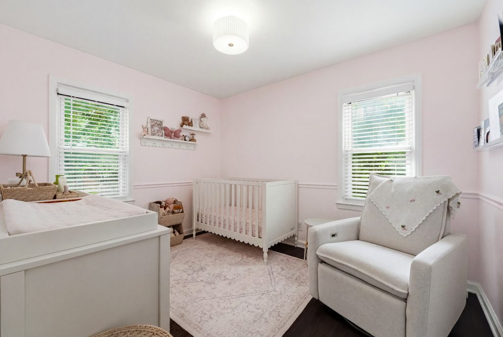 Pink nursery in a Royal Oak home with white crib, rocking chair, changing table, and two windows.