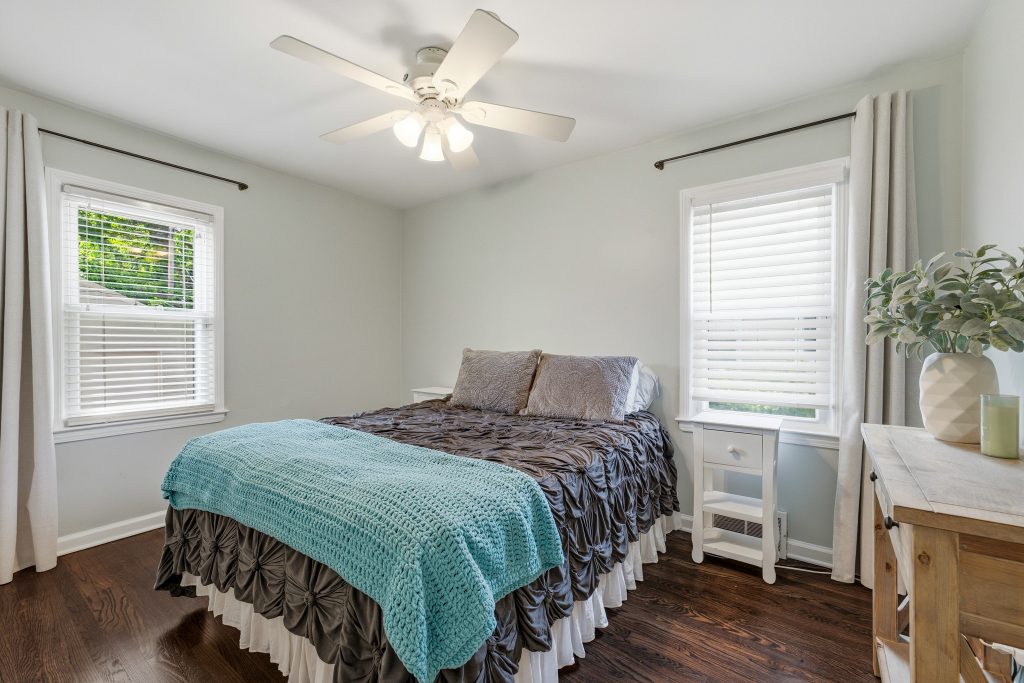 Main-floor bedroom in a Royal Oak home with hardwood floors, bed, two windows, ceiling fan, and light green walls.