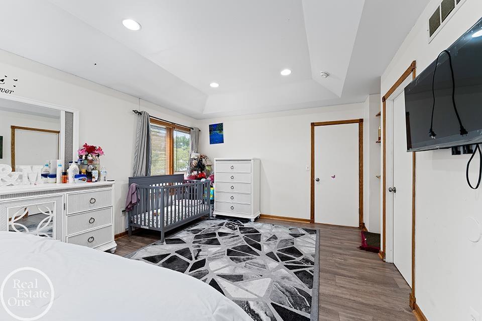 Bedroom at 22212 Mylls Ct in St. Clair Shores with tray ceiling, crib, dresser, large window, wood trim, and patterned rug.