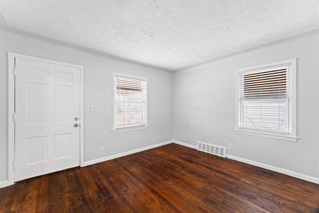 Vacant Eastpointe bungalow living room with hardwood floors, light gray walls, white trim, front door, and two windows.
