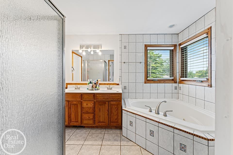 Bathroom at 22212 Mylls Ct in St. Clair Shores with soaking tub, shower, vanity, tile finishes, wood trim, and natural light.