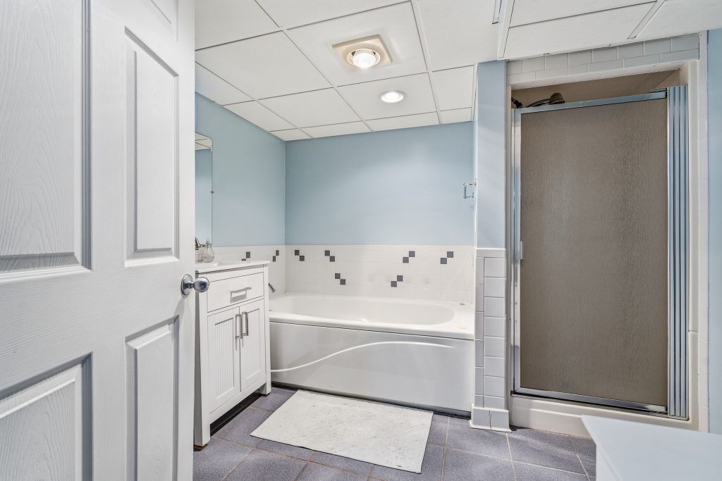 Basement bathroom in a Royal Oak home with jetted tub, separate shower, white vanity, blue walls, and tile flooring.