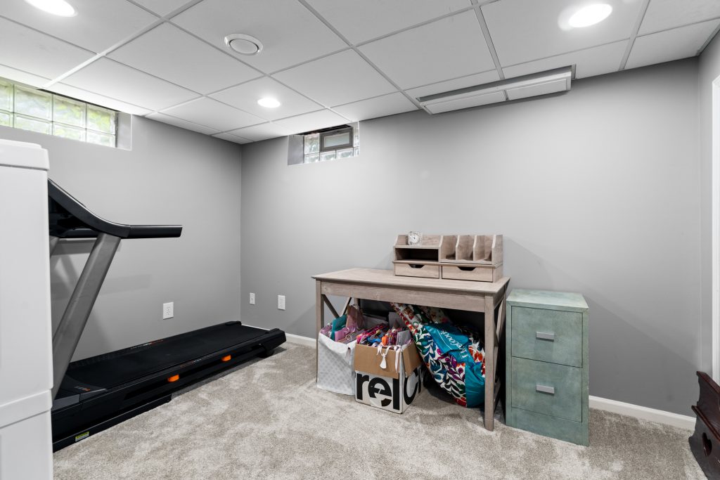 Basement flex room in a Royal Oak home with treadmill, desk, carpet, gray walls, and glass-block windows.