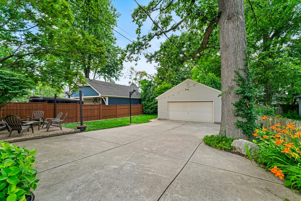 Royal Oak backyard with detached garage, concrete driveway, patio seating, lawn, mature tree, privacy fence, and landscaping.
