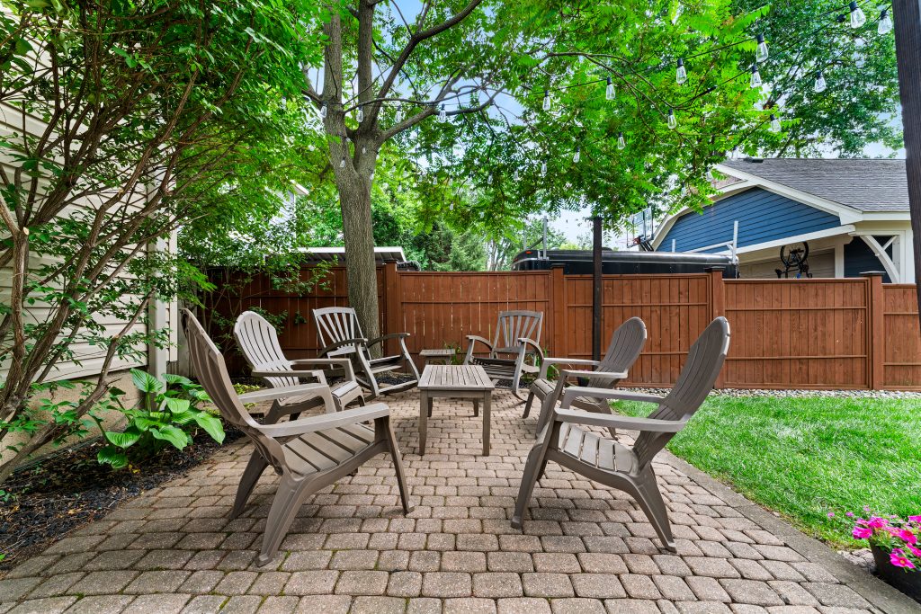 Shaded backyard patio in Royal Oak with outdoor chairs, brick pavers, string lights, mature trees, and wood privacy fence.