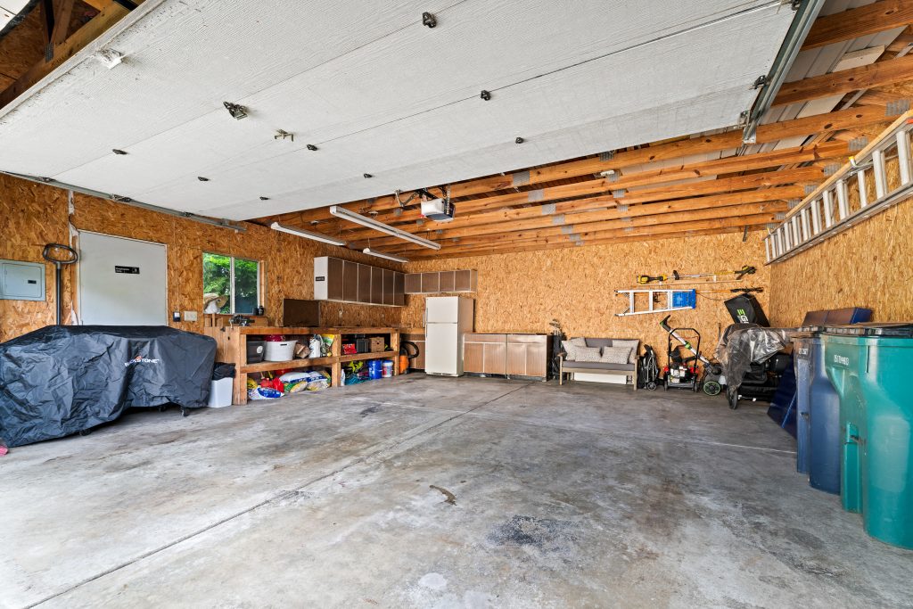 Interior of a detached Royal Oak garage with workbench, cabinets, refrigerator, tools, storage, and open concrete floor.