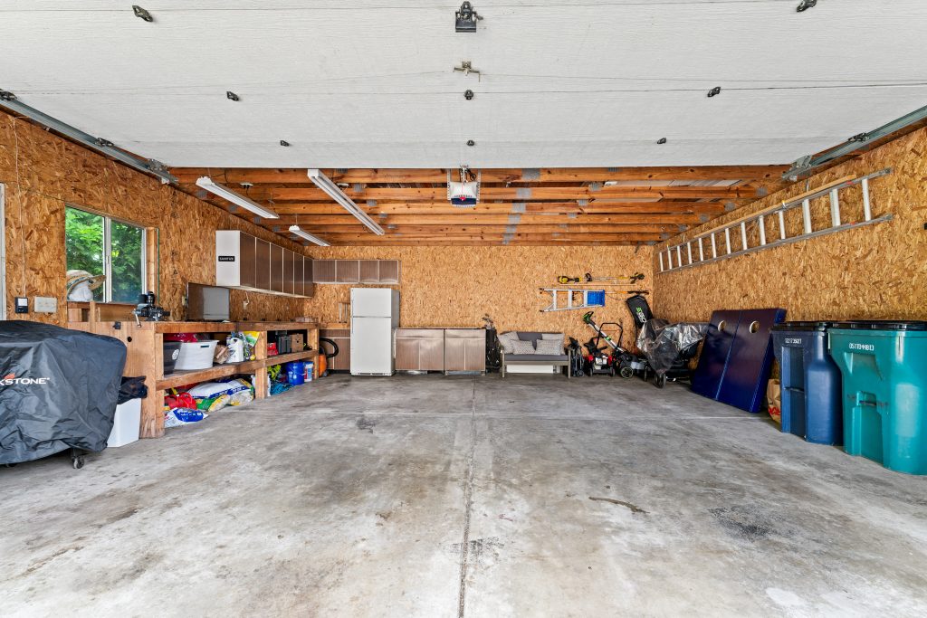 Wide interior view of a large detached garage in Royal Oak with exposed wood framing, storage cabinets, workbench, tools, and concrete floor.