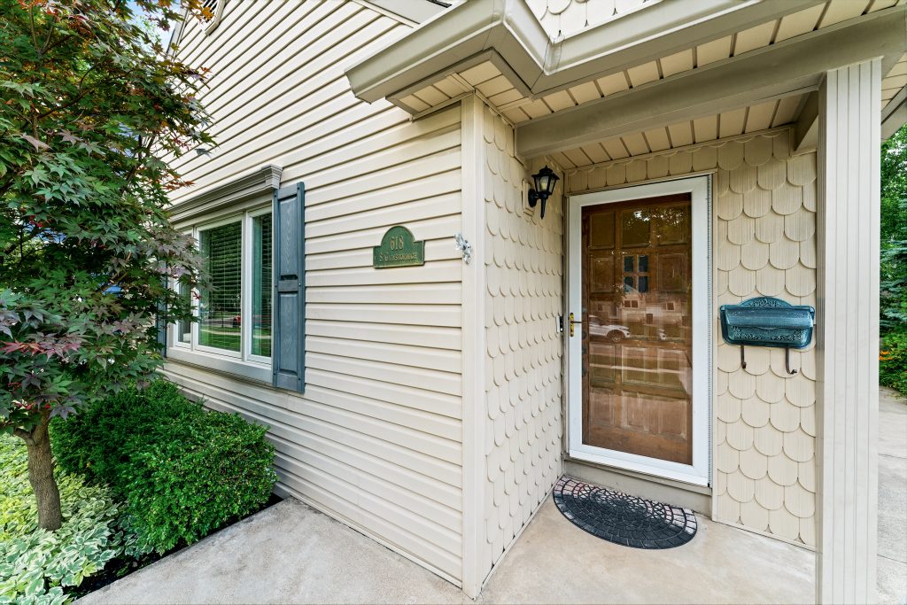 Covered front entry of a Royal Oak home with wood door, scalloped siding, address plaque, mailbox, and landscaping.