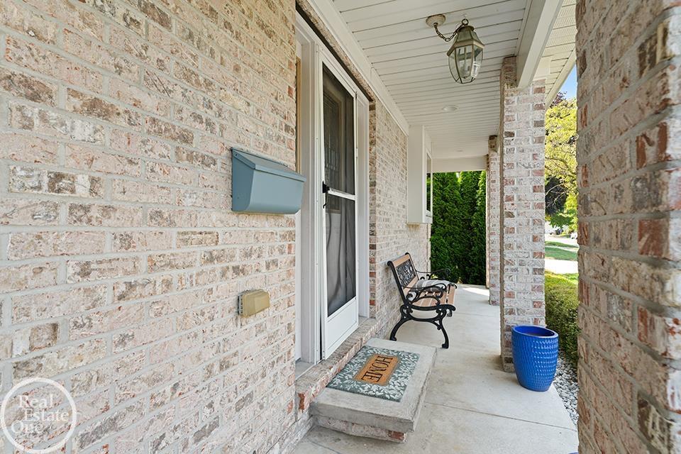 Covered porch of a St. Clair Shores home with brick columns, blue planters, front door, and bench.
