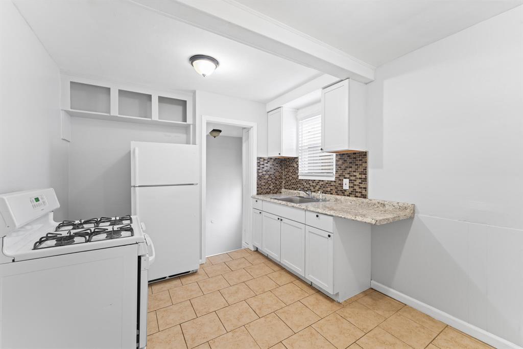 Compact Eastpointe kitchen with white cabinets, peninsula counter, white appliances, mosaic backsplash, and tan tile floor.