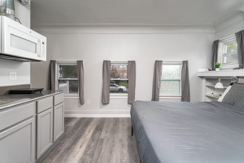 Detroit guest suite with three windows, gray kitchenette, large bed, built-in shelving, and neutral interior finishes.