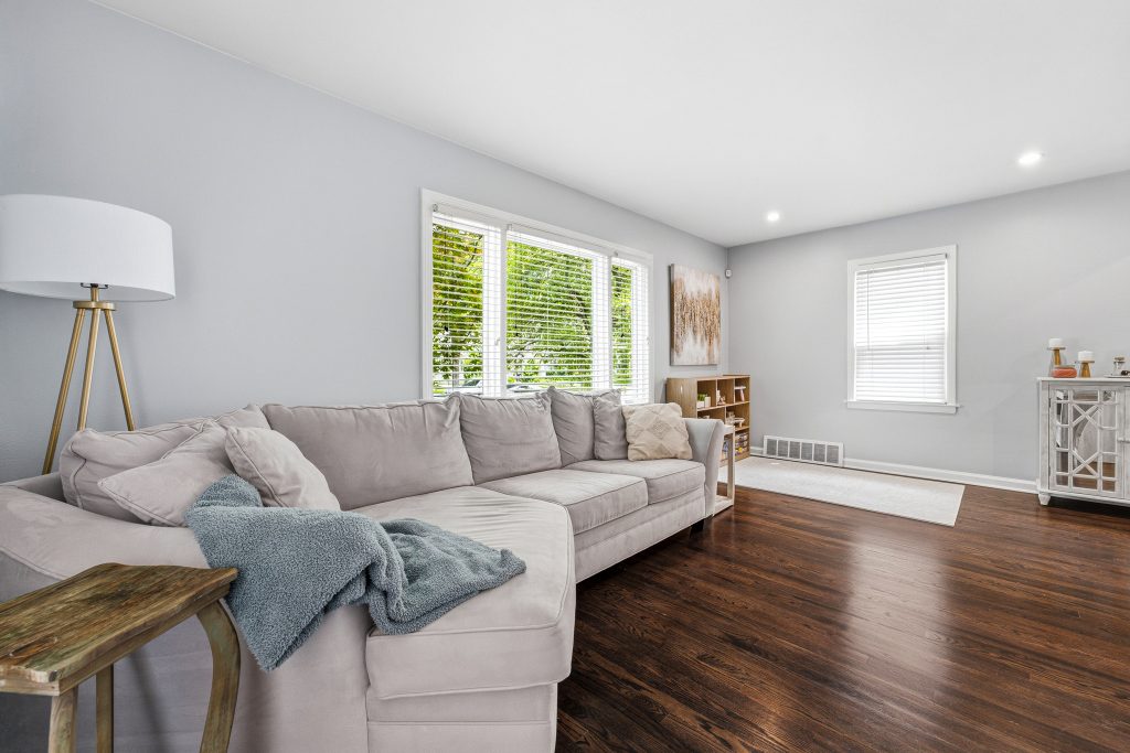 Bright Royal Oak living room with dark hardwood floors, large front windows, gray walls, and sectional sofa.