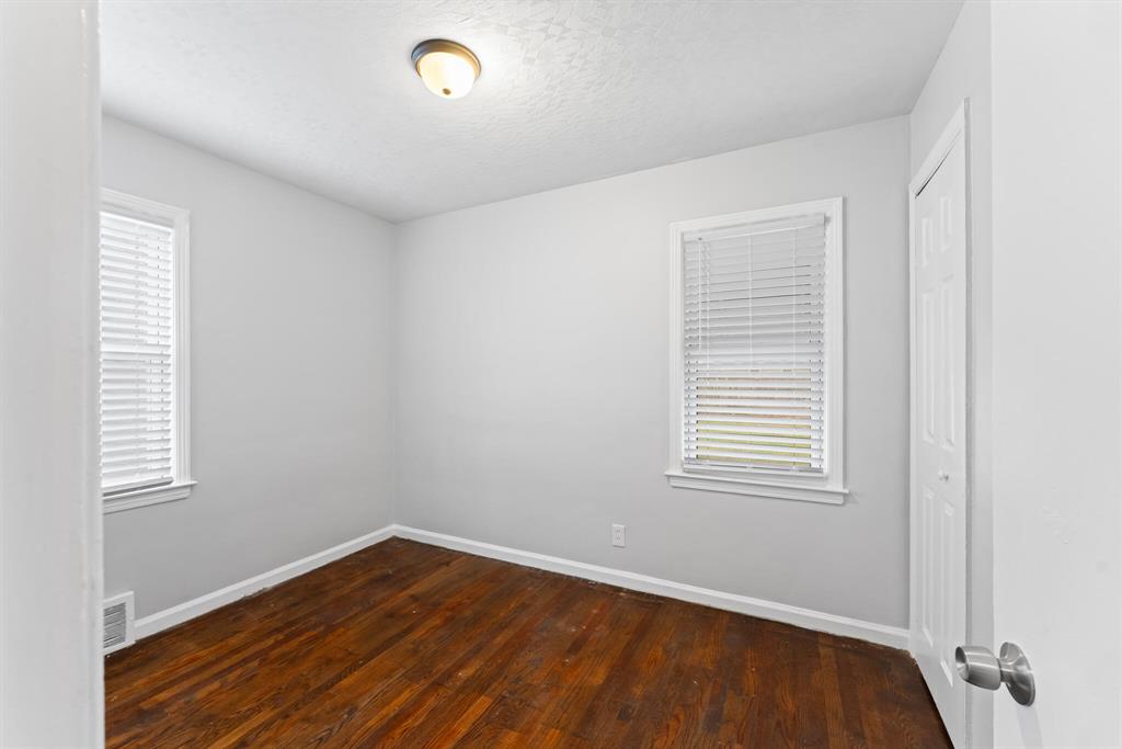 Vacant bedroom with two windows, hardwood floors, pale gray walls, white trim, and a paneled closet door.