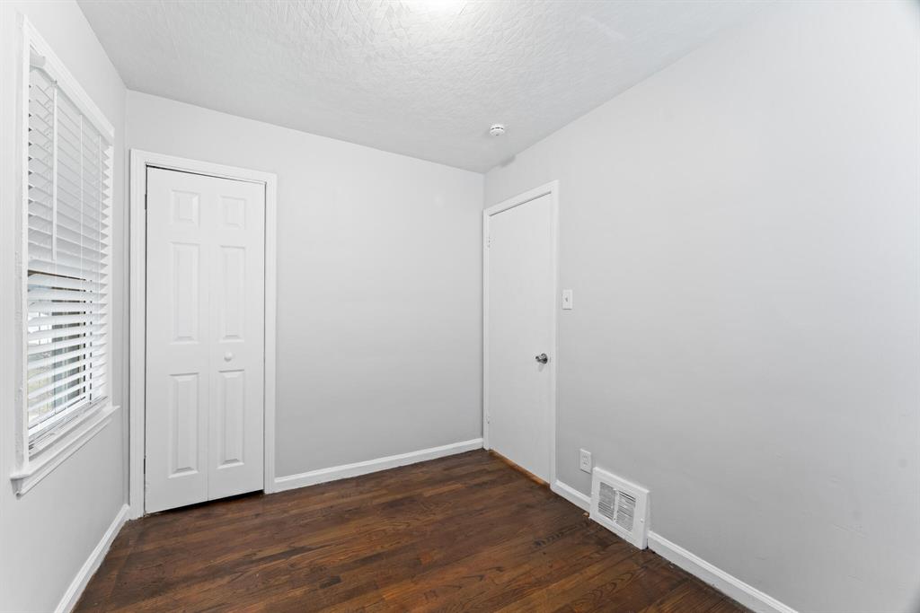 Compact bedroom with hardwood flooring, side window, double closet doors, gray walls, and white trim.