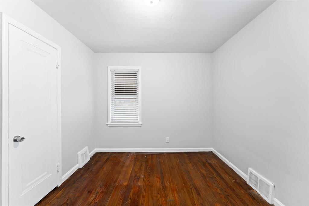 Long narrow bedroom with one window, hardwood floors, light gray walls, white trim, and a paneled door.