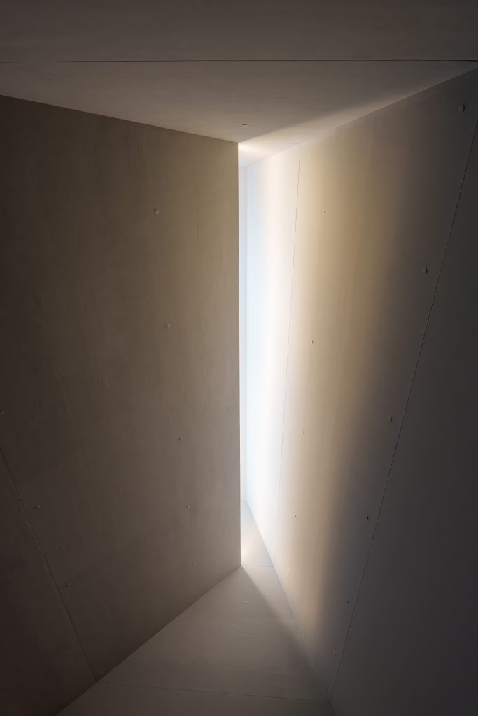 Angular architectural surfaces frame a narrow opening of natural light inside the Frederik Meijer Gardens Welcome Center.