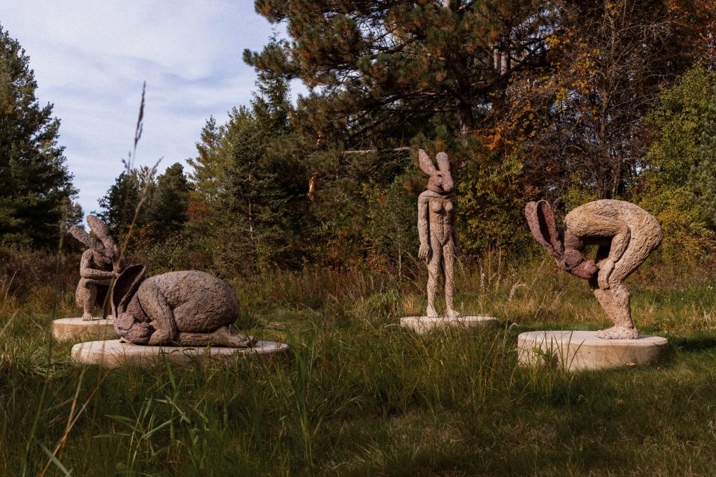 Four textured bronze figures with hare-like heads gather in Sophie Ryder's Introspective sculpture among garden vegetation.