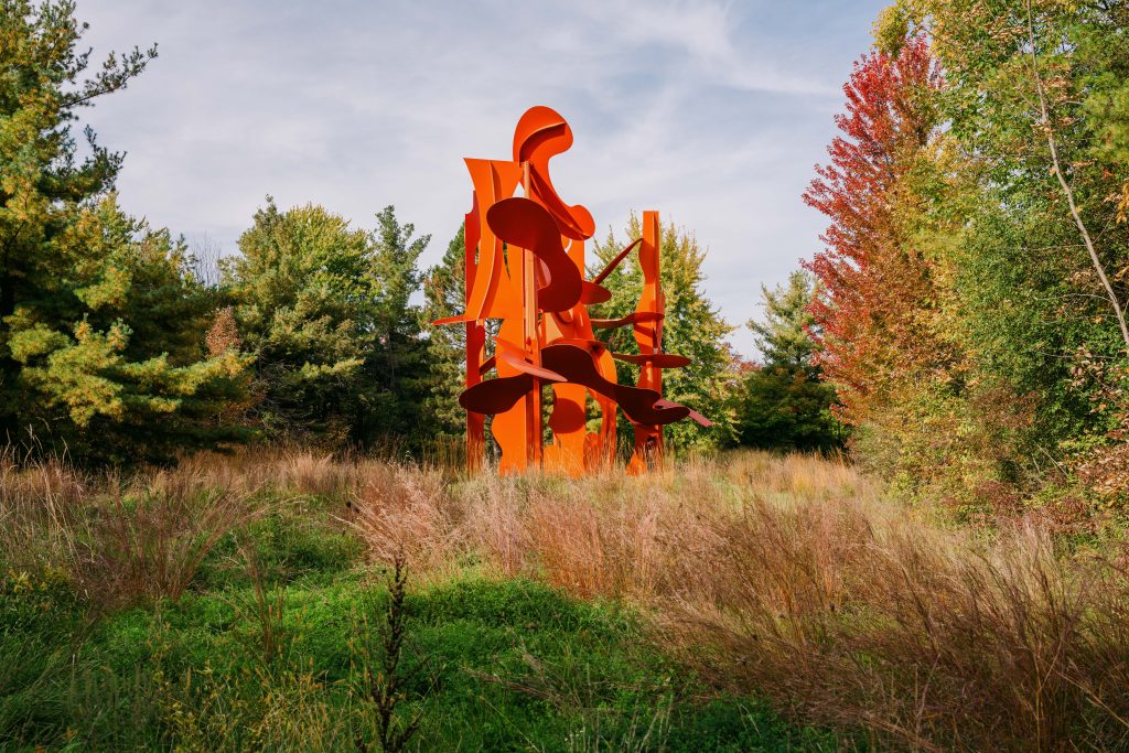 Vivid orange-red painted steel curves rise above golden meadow grasses in Alexander Liberman's monumental Aria sculpture.